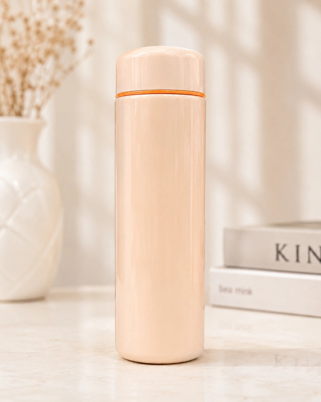 Beige thermos bottle with orange top on a light surface