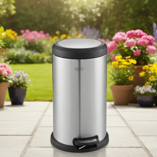 Silver trash bin with black lid on a patio with flowers in the background