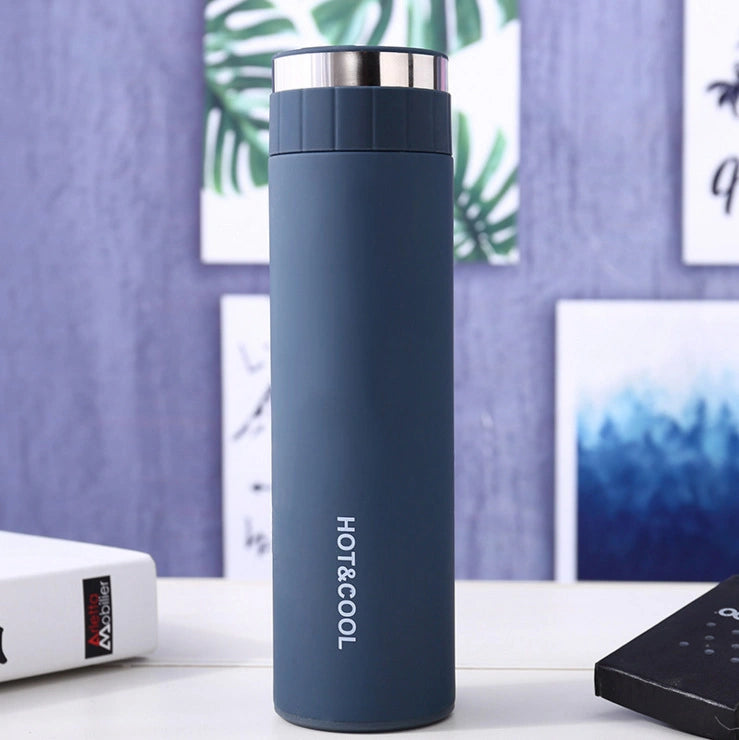 Blue thermos bottle with 'HOT&COOL' text on a desk with a purple wall and plant in the background