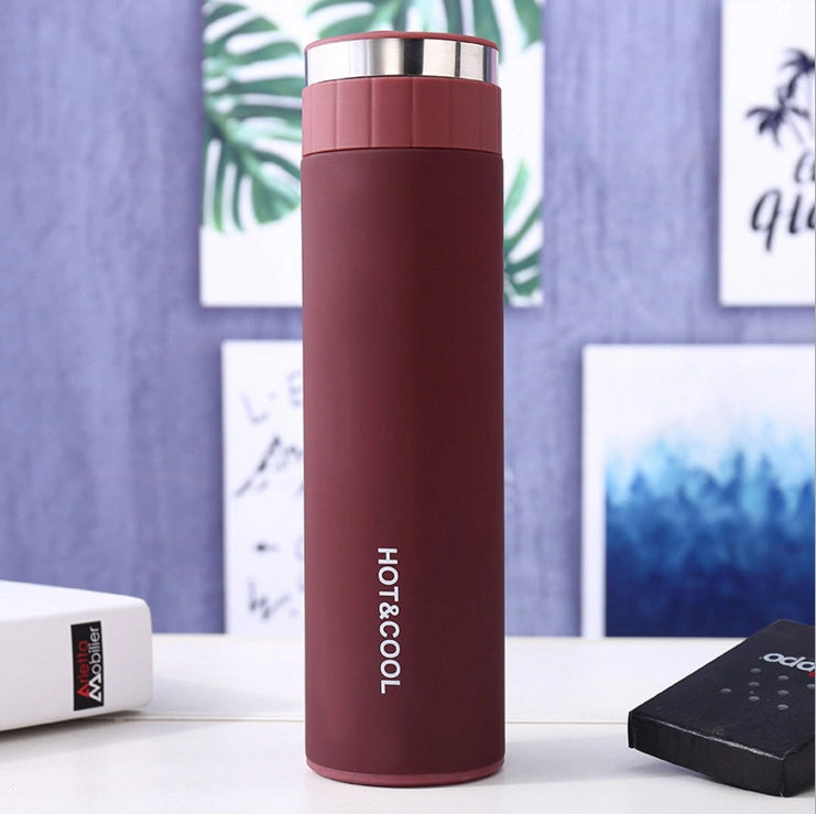 Maroon thermos bottle with 'HOT & COOL' text on a blurred indoor background