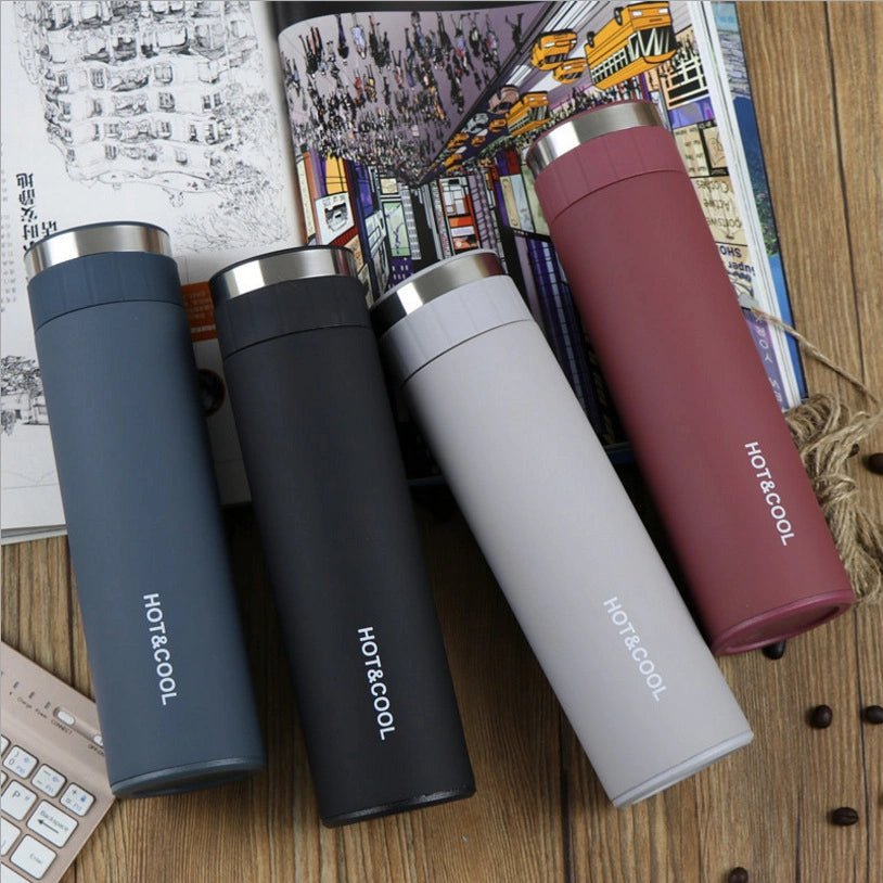 Four insulated travel mugs in different colors on a wooden surface with a magazine in the background.