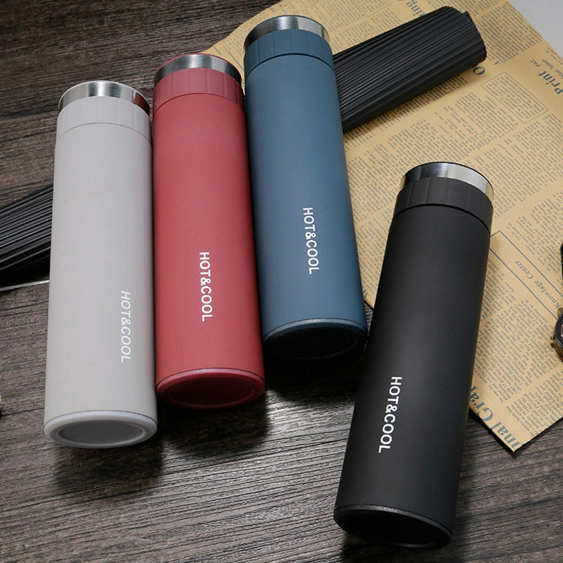 Four thermos bottles in different colors on a wooden surface with a newspaper underneath.